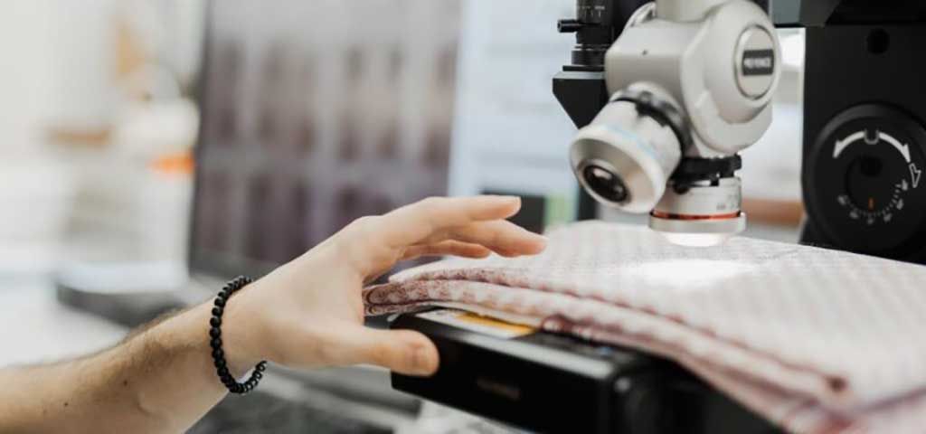 A textile specialist inspects fabric under a digital microscope to evaluate its texture, weave, and overall material quality before production. Garment construction shapes product value in premium clothing.