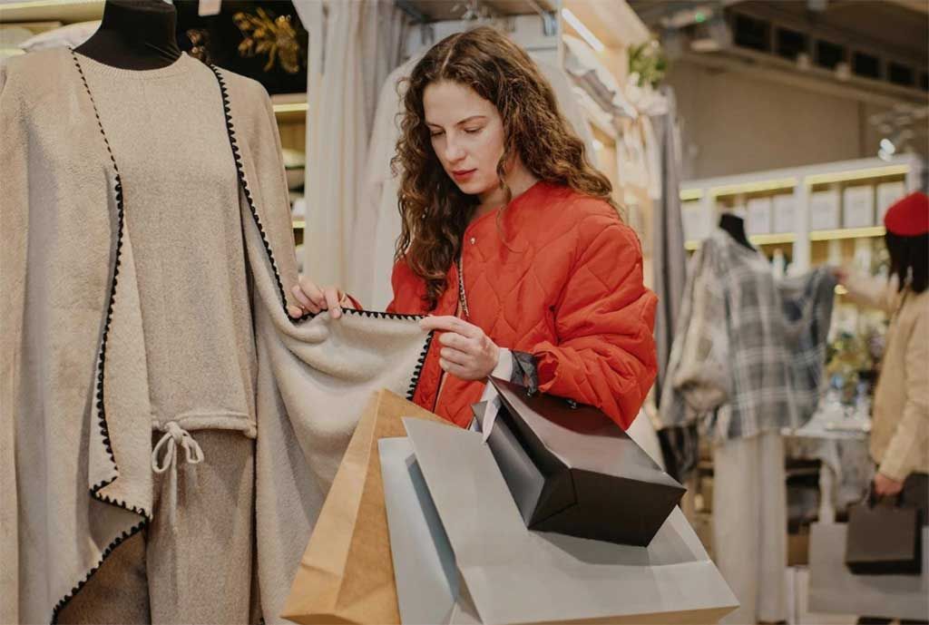 A shopper examines the fabric and construction of a garment while browsing in a clothing store. Consumers evaluate garment construction&nbsp; by inspecting materials, stitching, finishing details, and overall presentation.