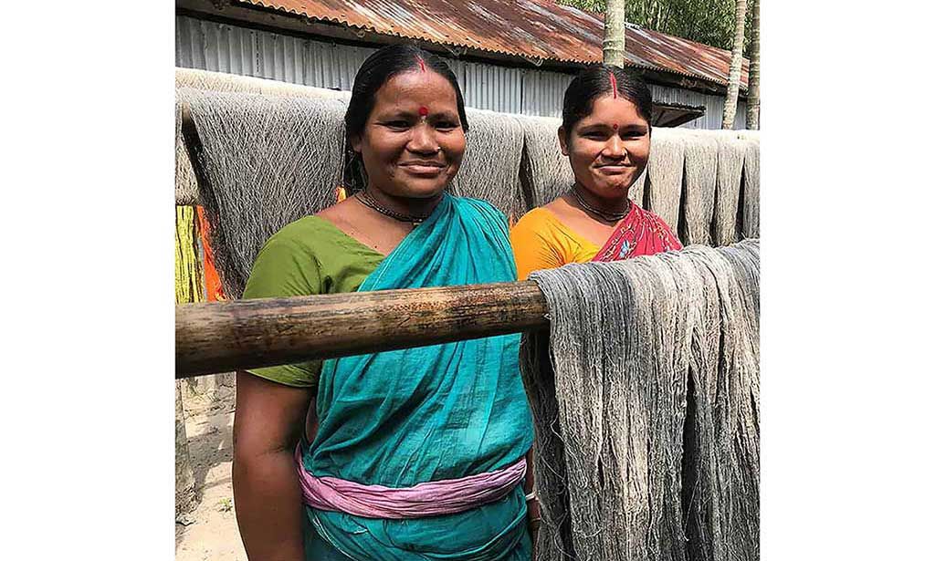 Two Bangladeshi women standing amongst yarn to be used by Motif Handmade in handweaving sustainable fabrics.